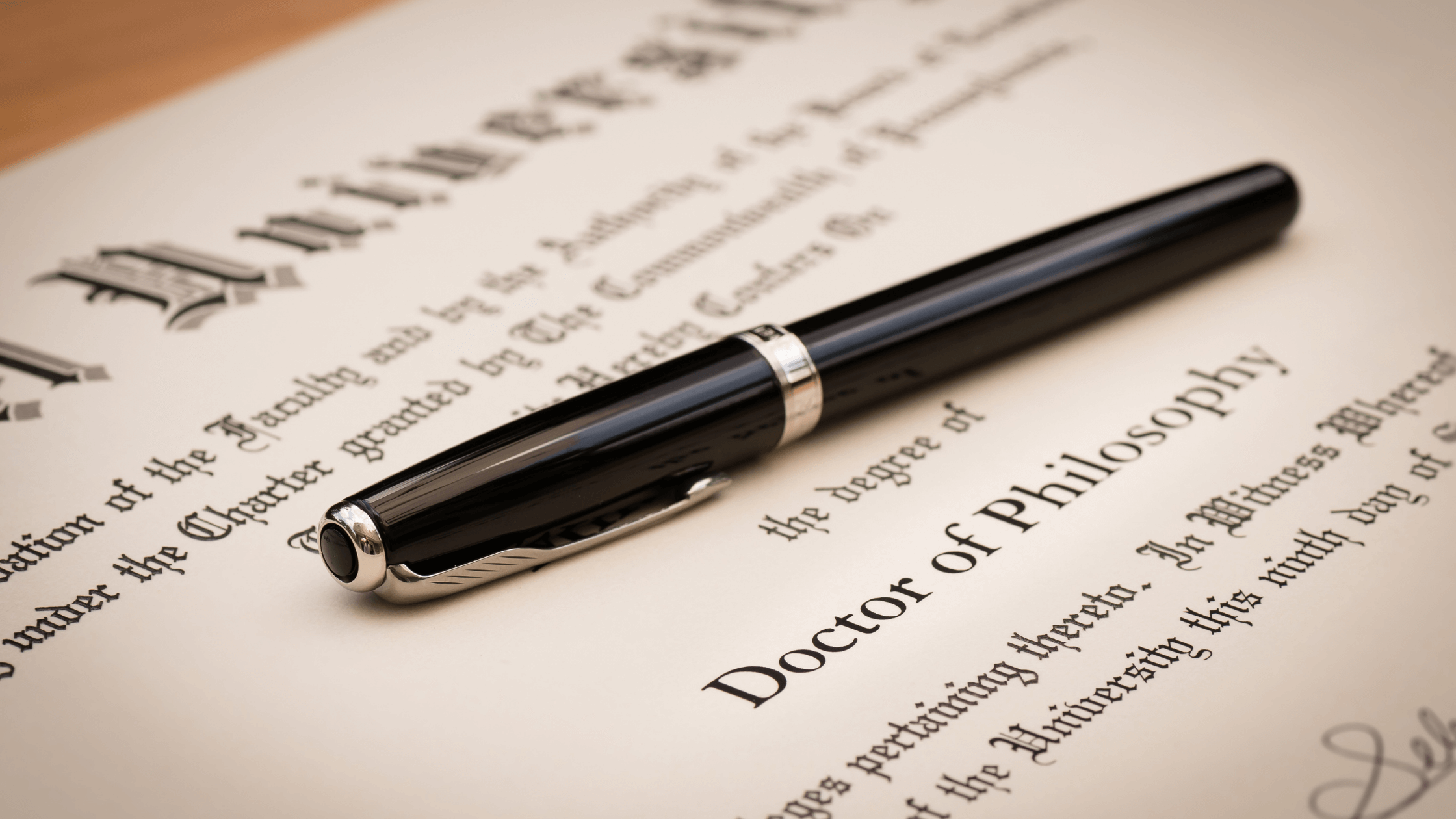A black and brass gel pen sitting onto of a doctorate of philosophy diploma from a university