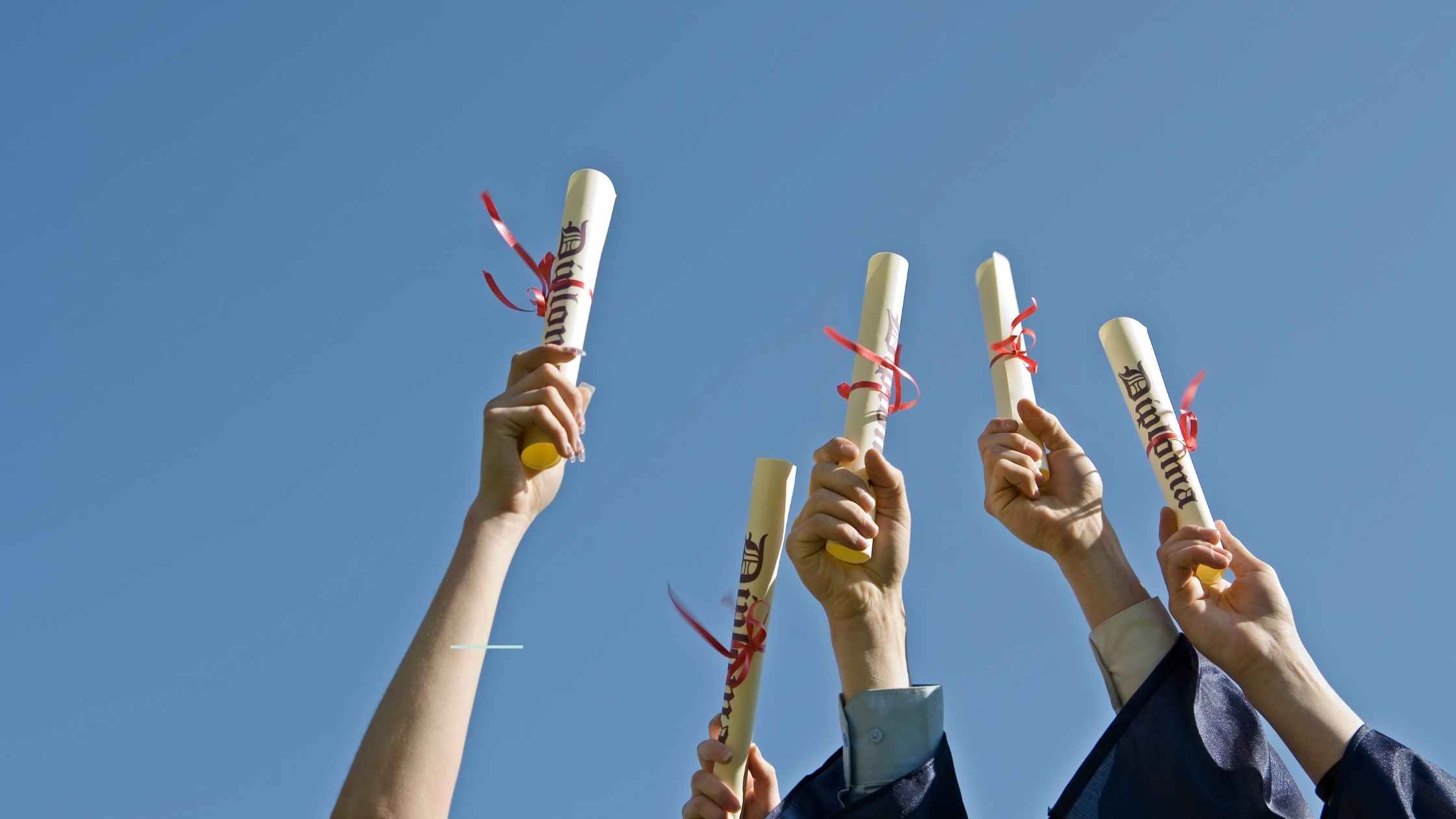 holding up high school graduate diplomas to the blue sky