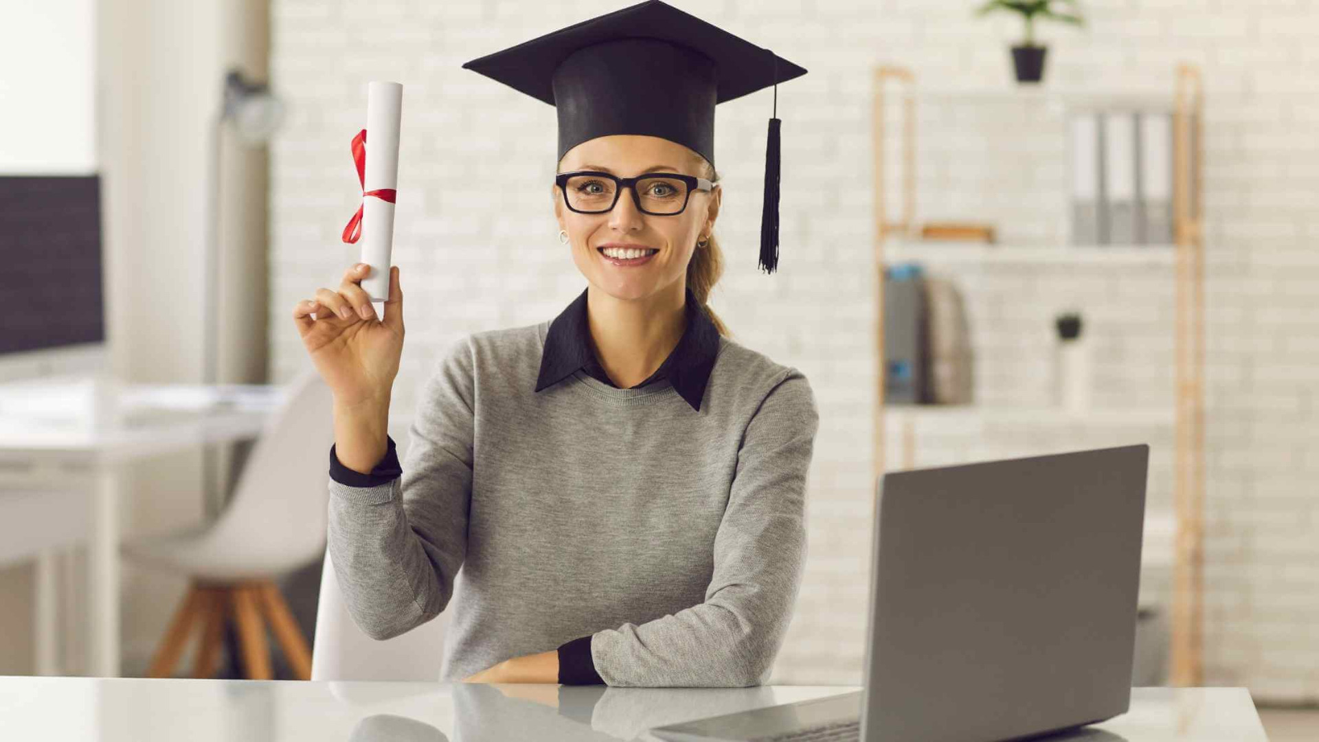 smiling woman with glasses next to laptop in graduate cap buying diplomas online 