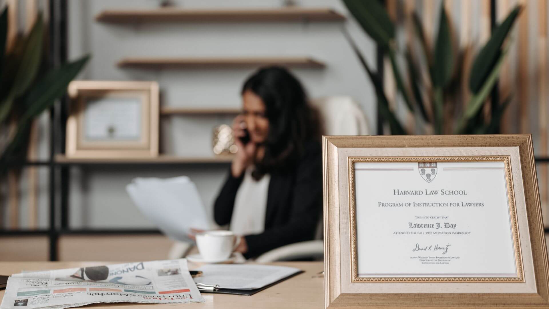woman on phone at desk with harvard law school diploma in the distance