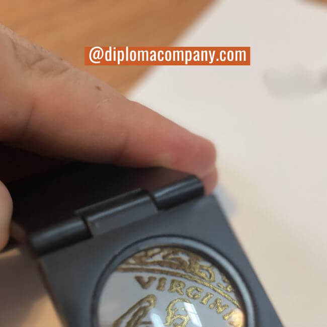 Finger touching raised embossed gold metallic seal on replica diploma showing physical texture and depth